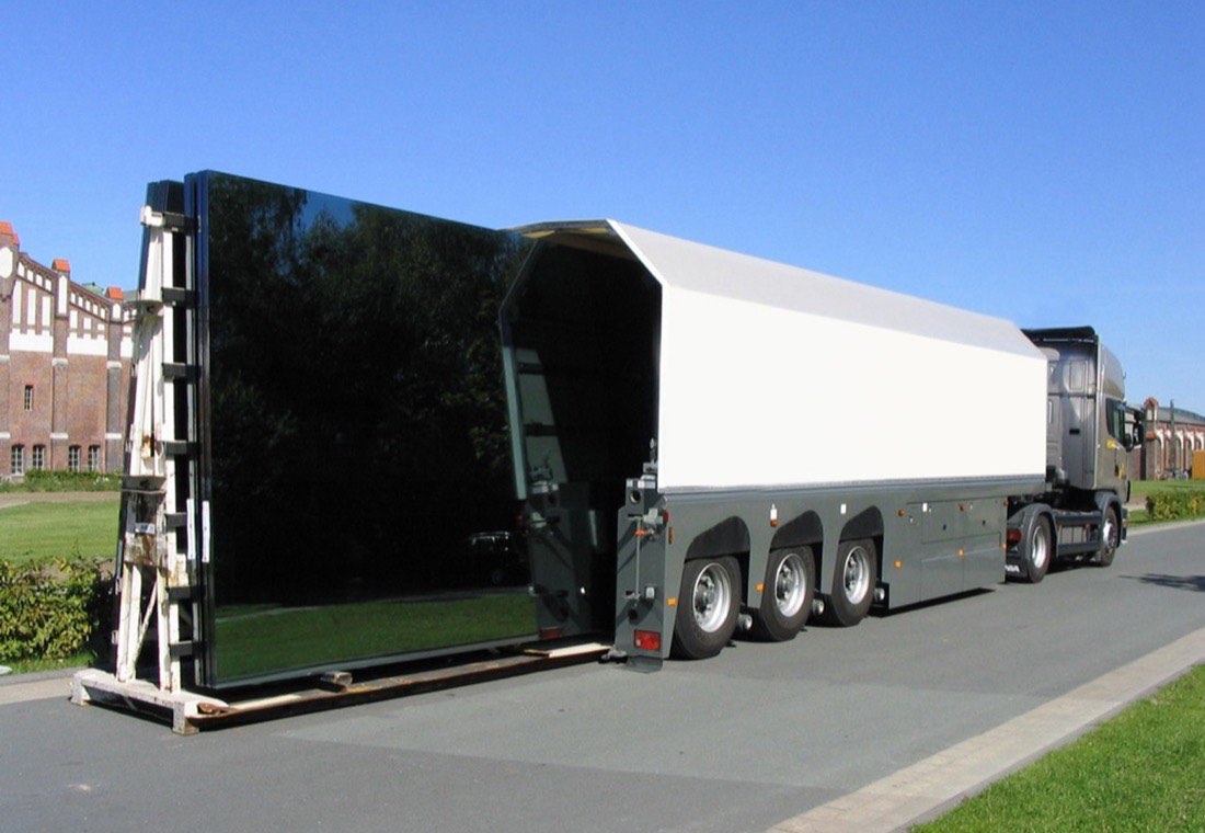 Semi-remorque de transport de vitrage en cours de déchargement de grands panneaux de verre
